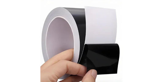 Hand peeling black adhesive light blocking tape from a roll on white background