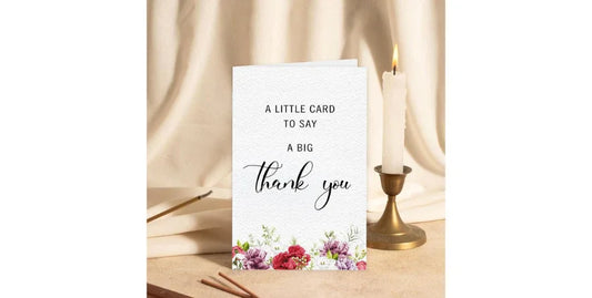 Thank you card with floral design beside lit candle and beige fabric background